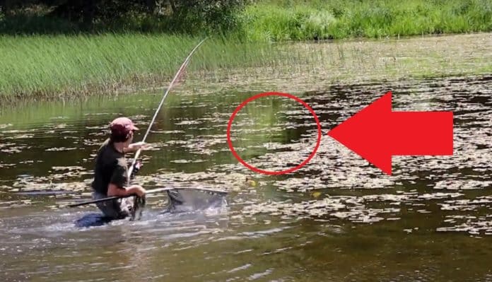 Mladý rybář zdolává ryby na zarostlém rybníku