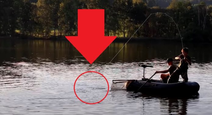 Rybář zdolává rybu na rybníku z rybářského člunu