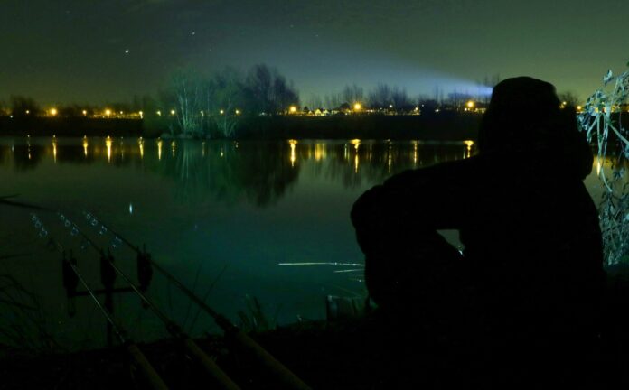 Rybář svítí čelovkou na hladinu při nočním rybaření