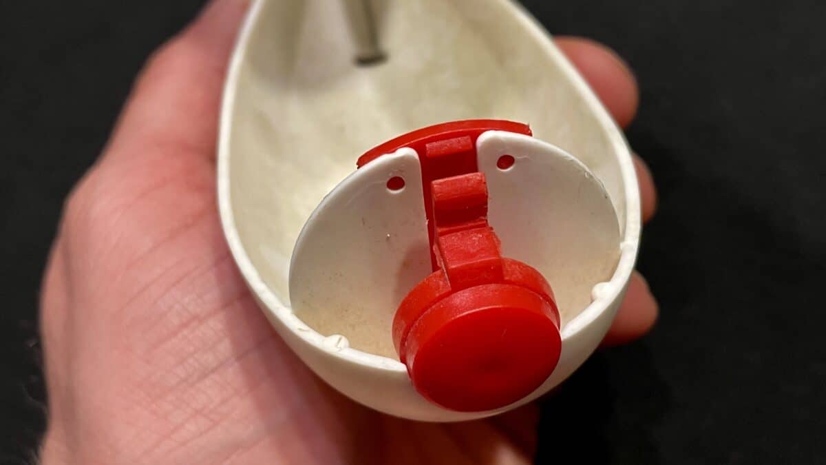 Close-up of a white plastic device with a red hinge/gear, held in a hand against a dark background.