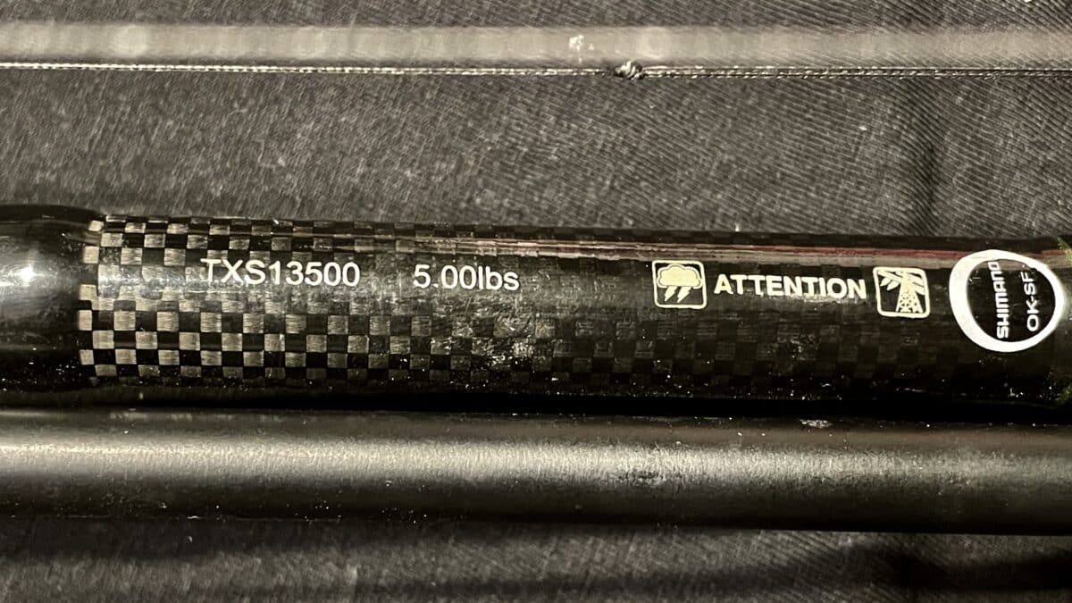 Close-up of a carbon fiber bicycle frame tube with the label TXS13500 and a 5.00 lbs weight rating, plus attention icons and Shimano OK sticker.