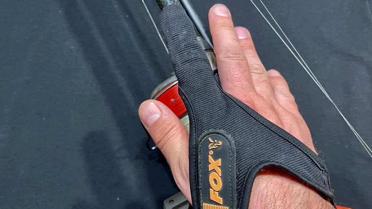 Close-up of a hand gripping a black fabric strap with orange branding around a red cylindrical tool against a dark background.