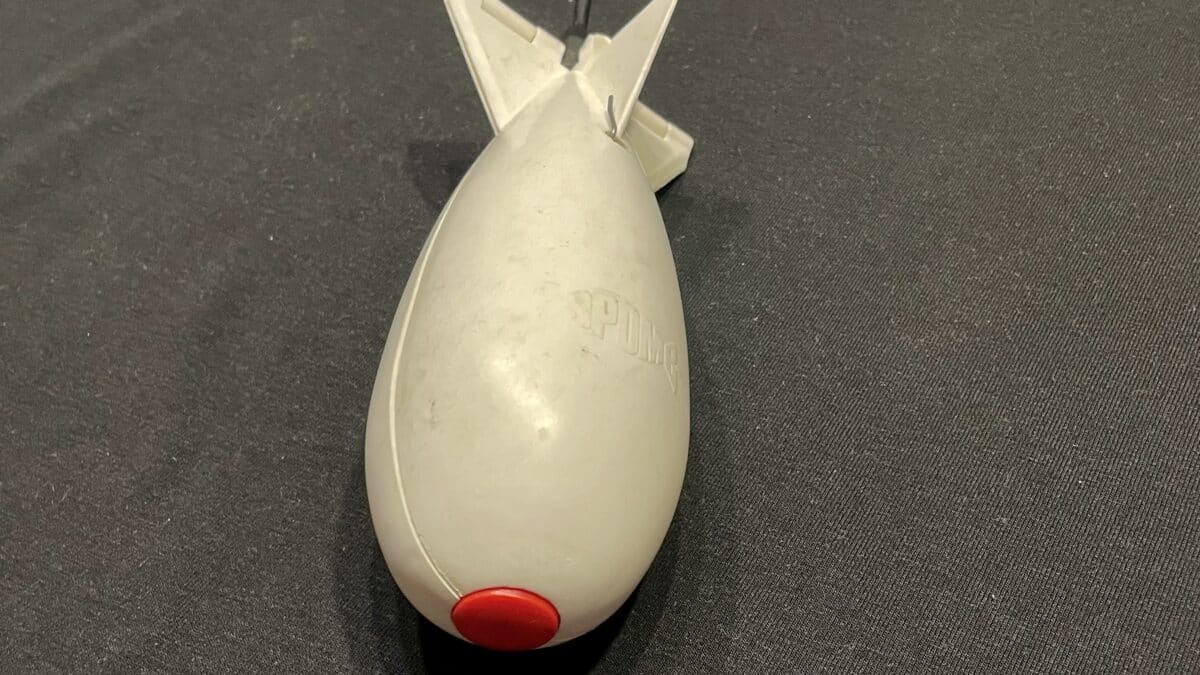 Gray handheld plastic device with a red circular button at its end, resting on dark fabric.