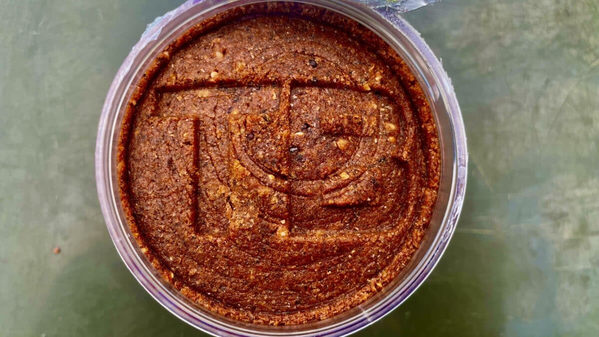 Top-down view of a dense brown cake with nuts in a round glass jar, seen from above in warm lighting.
