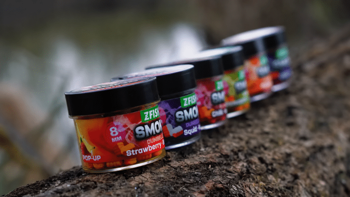 Row of colorful ZFISH gummy candy jars lined up on a rough outdoor wooden/rocky surface, foreground shows Strawberry flavor.