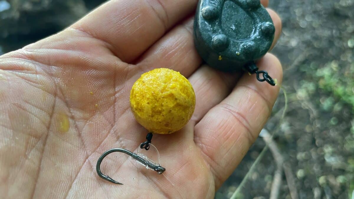 Close-up of a bright yellow, round fishing bait attached to a small hook, held in a palm.