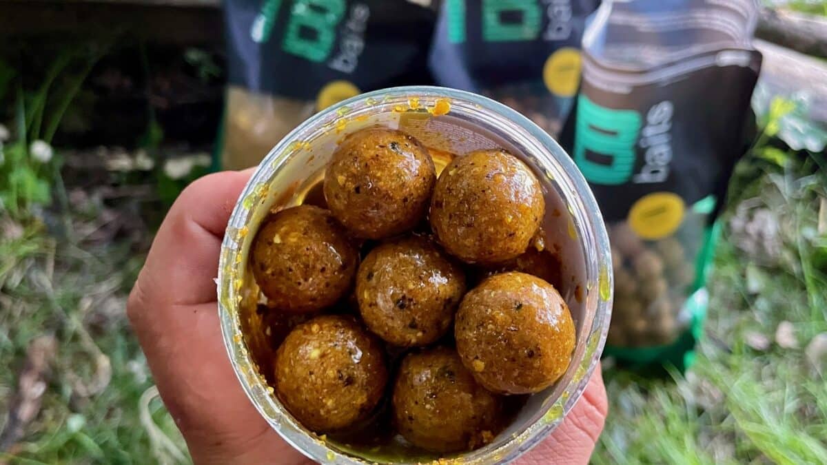 Hand holding a clear jar filled with brown, spice-coated round snack balls.