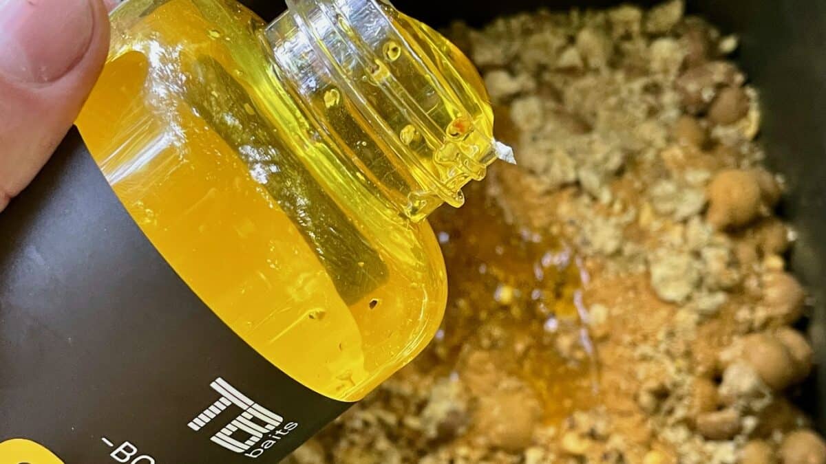 Close-up of a yellow oil bottle being squeezed over a pan with browned ground meat and sauce.