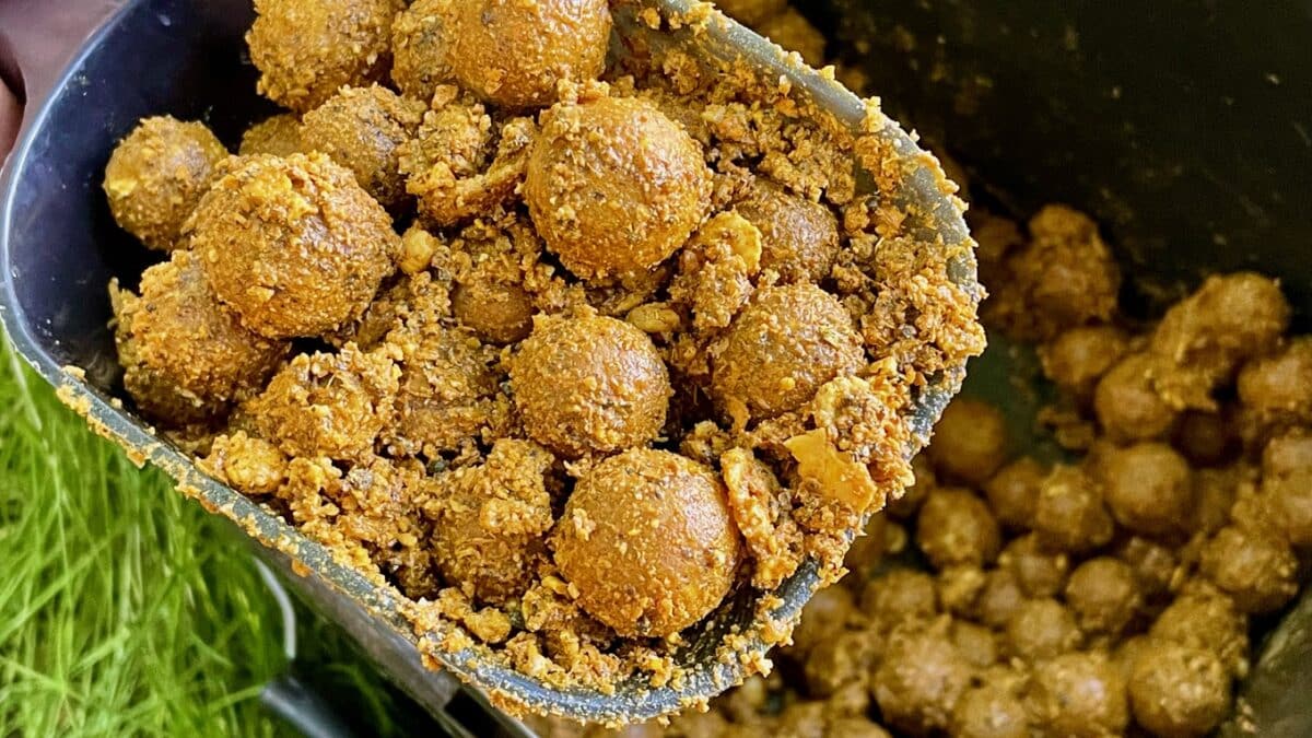 Close-up of fried Indian laddus (laddoo) with a crumbly coating in a scoop and tray of more laddus nearby