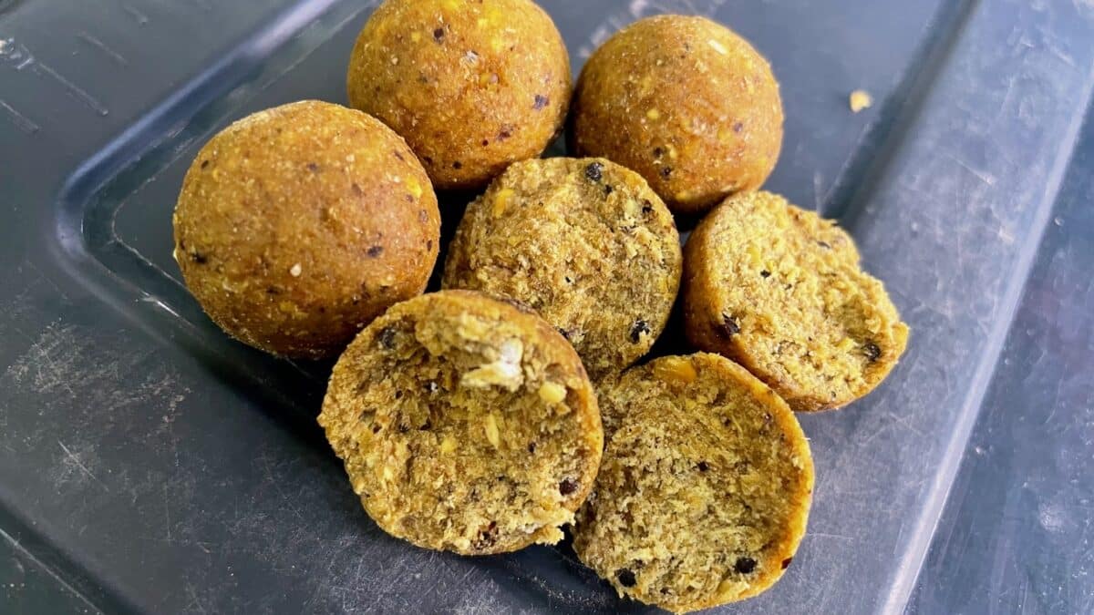 Eight golden-brown snack balls on a dark tray; one or two are halved to show a crumbly, nut-studded interior.