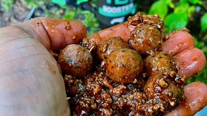 Close-up of dirty brown clay pellets held between fingers outdoors.