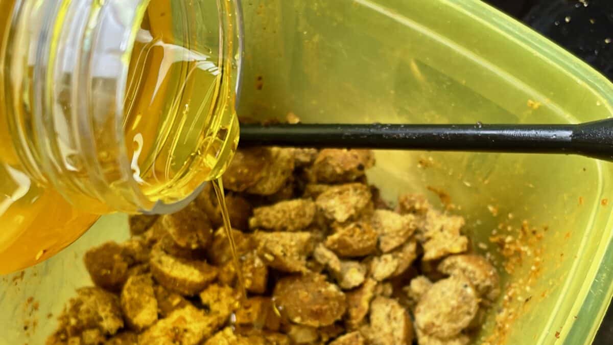 Close-up of honey being poured from a jar onto granola in a yellow bowl with a green rim.