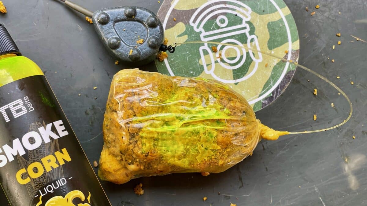 Close-up of a yellow-green plastic bag with chunky contents next to a vape-liquid bottle and a gray circular device on a dark surface with a camo target logo in the background.