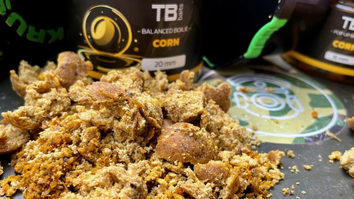 Close-up of chunky granola clusters on a tray with blurred bottles in the background, showing a crumbly, toasted snack texture