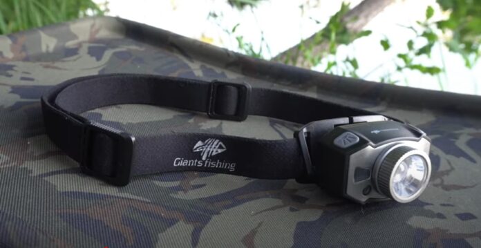 Headlamp with an adjustable black strap labeled Giants Fishing on a camo surface, outdoors.