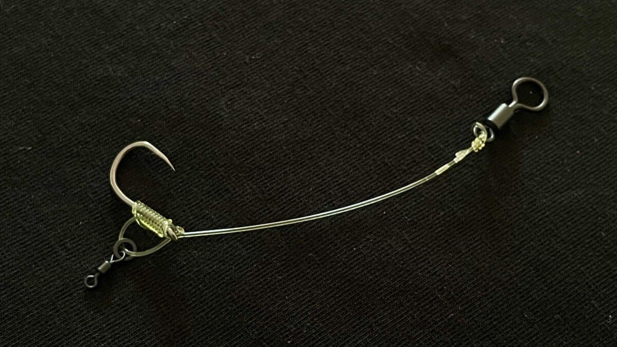 Close-up of a fishing rig with two curved metal hooks connected by a wire leader on a dark fabric background.