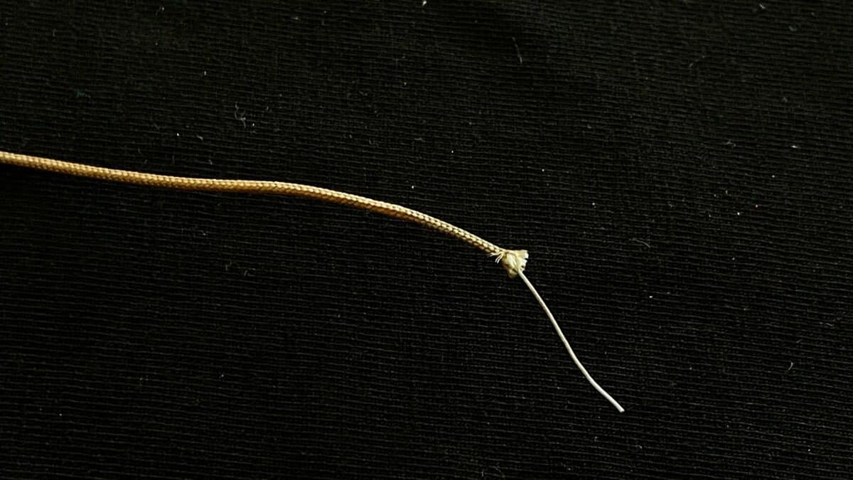 Close-up of a thin gold braided cord with a small knot on a white thread against a black textured background, seen horizontally across the image.