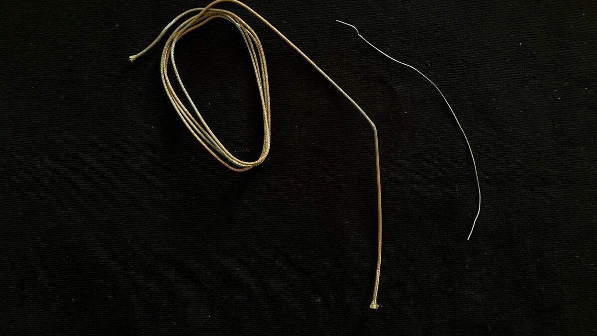 Beige braided cords looped on a black fabric surface with a single loose white thread nearby.