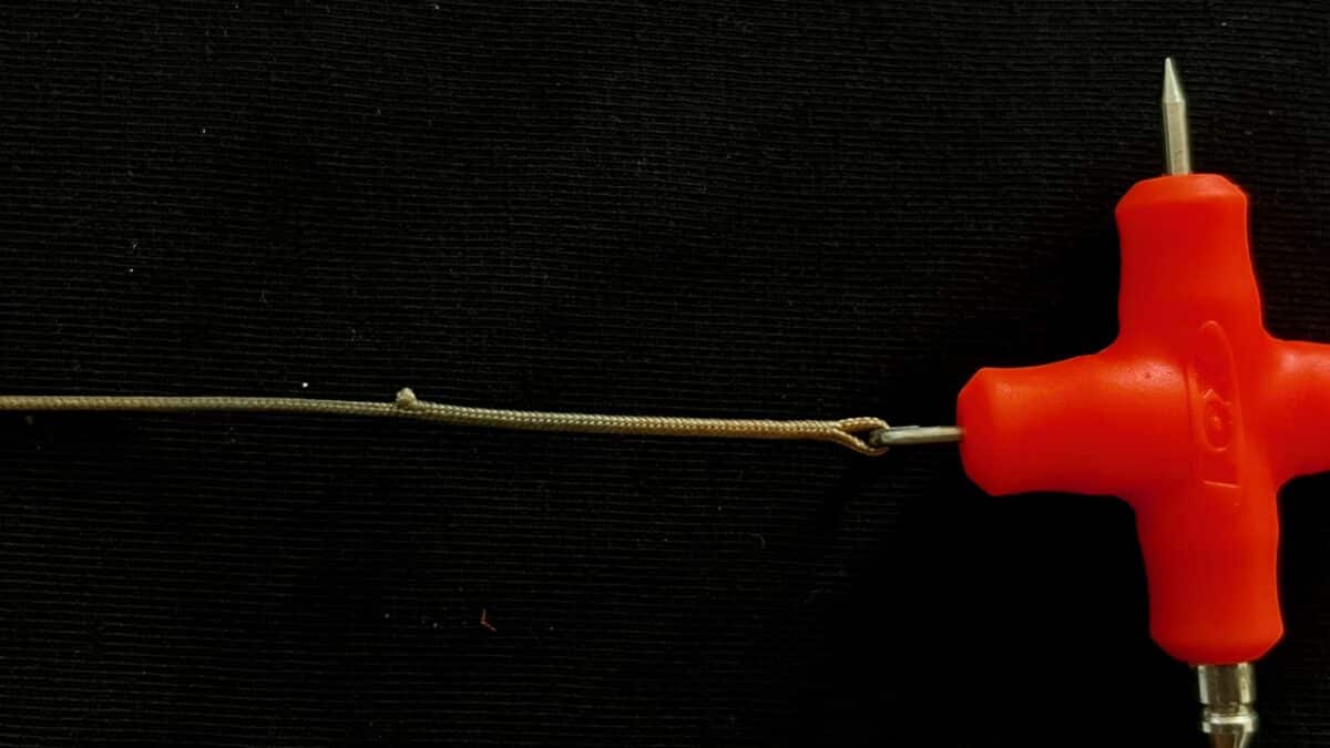 Close-up of an orange-handled screwdriver with a metal shaft on a dark textured background, a rope running horizontally across the frame.