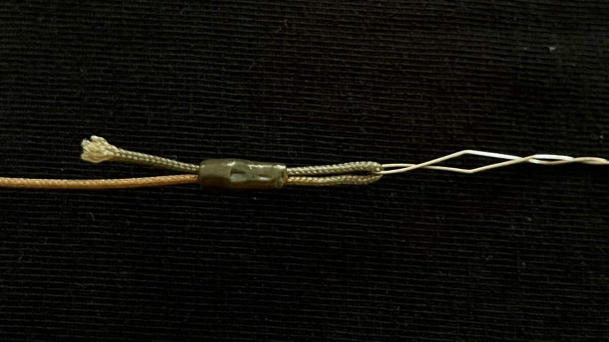 Close-up of a damaged electrical wire with exposed copper strands and a small plastic splice sleeve on a dark background