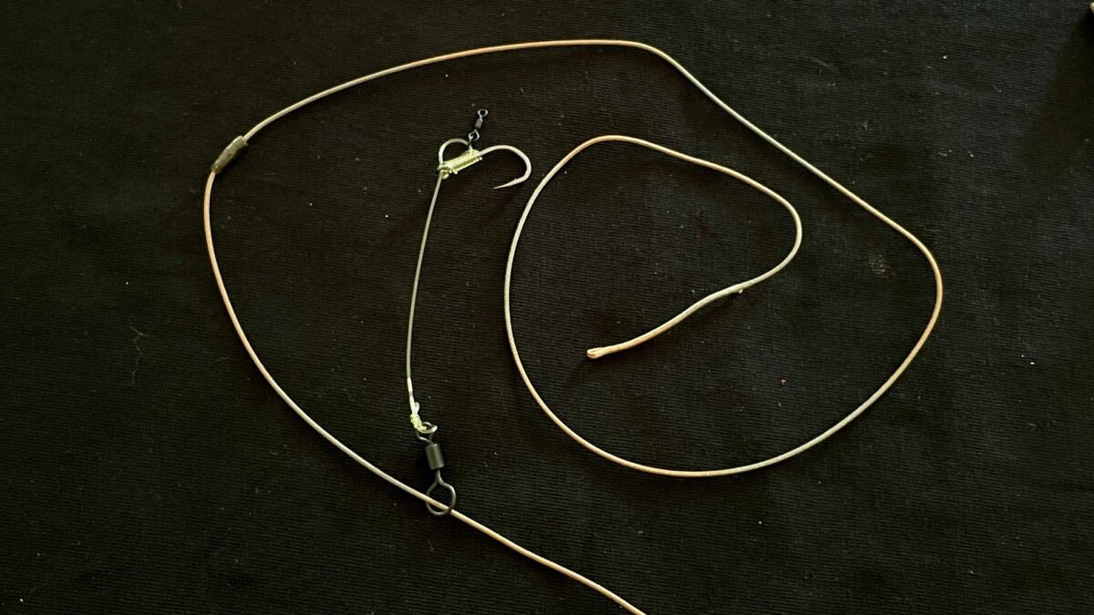 Brown cord necklace with metal clasps and small hooks laid on a dark fabric background.