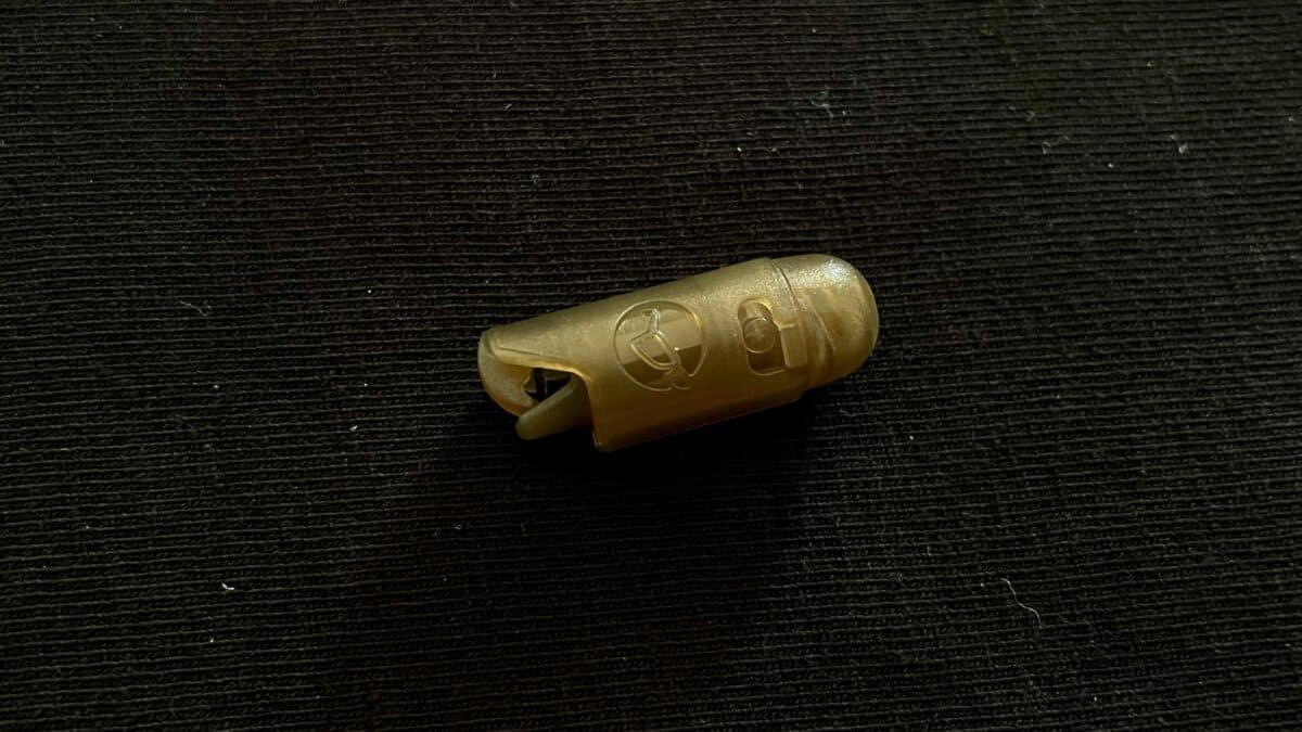 Small translucent beige plastic fastener or end cap with a curved prong, resting on black fabric texture.