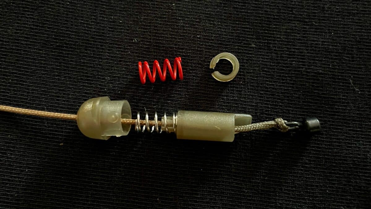 Close-up of a small red coil spring with plastic and metal parts on a dark surface, likely a disassembled mechanical component.