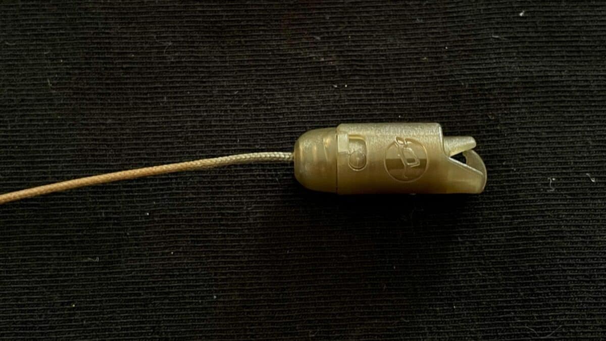 Beige plastic drawstring cord lock with a light cord threaded through, resting on dark fabric.
