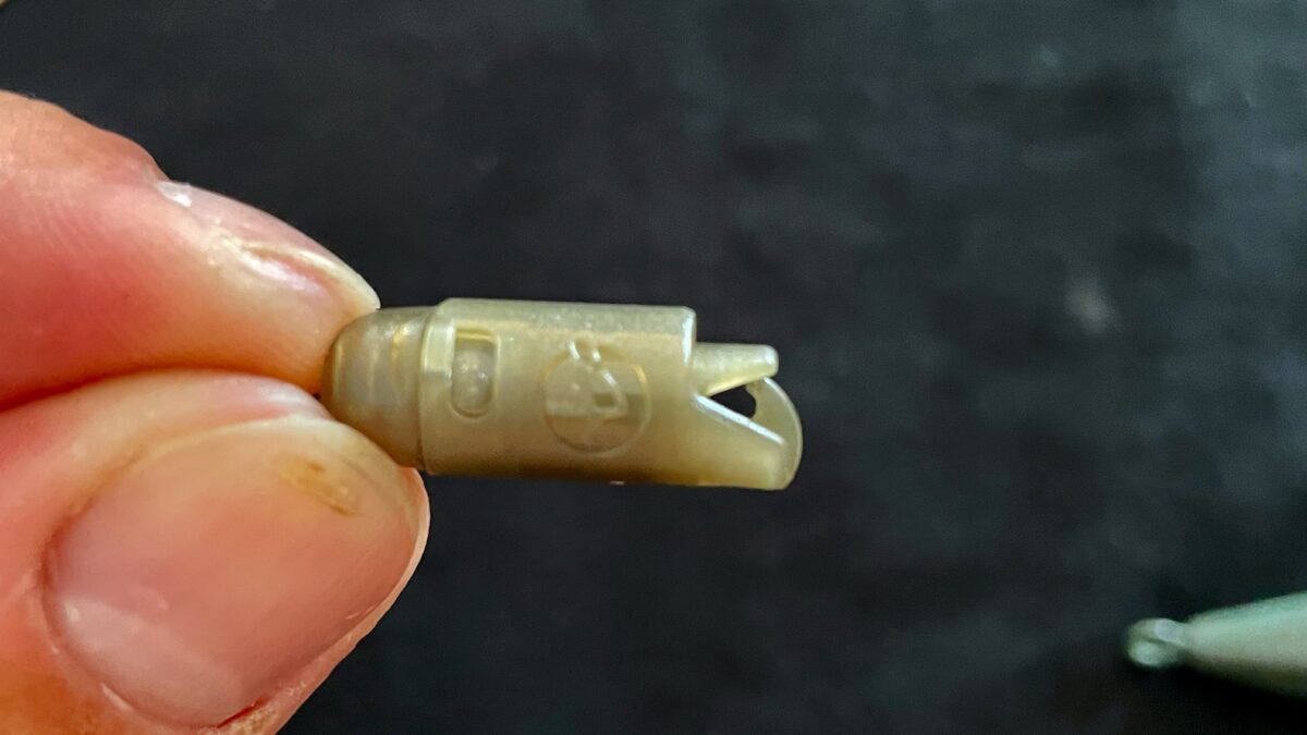 Close-up of a small beige plastic connector with a clip being held between fingers, showing a raised logo on the side.