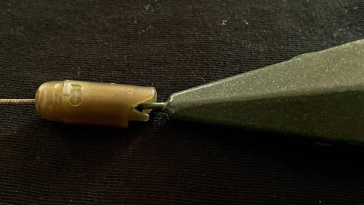 Close-up of a beige plastic electrical connector clamped to a wire beside a flat metal blade on a dark surface.