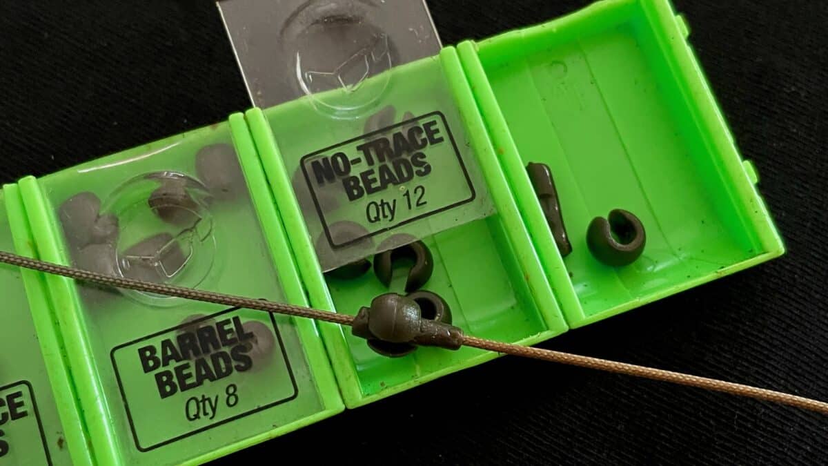 Green plastic fishing tackle box with labeled compartments for beads (No-Trace Beads, Qty 12) and beads visible inside the clear lids.