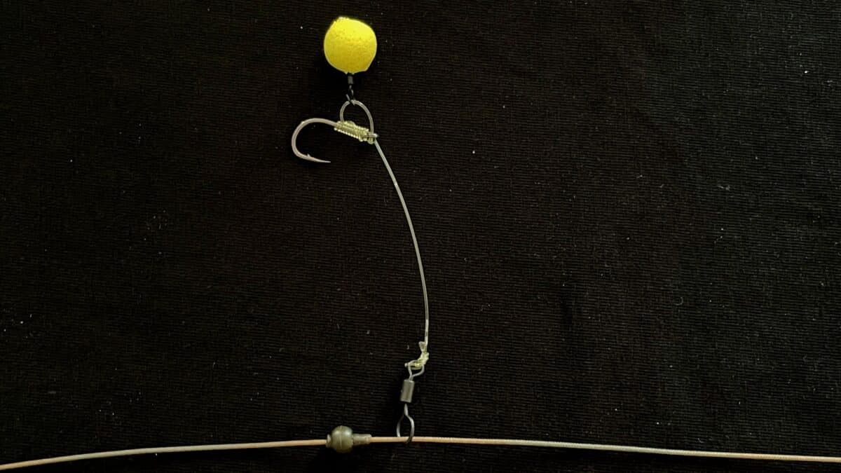 Close-up of a fishing rig with a yellow bead, hook, and leader against a dark background (fishing tackle).