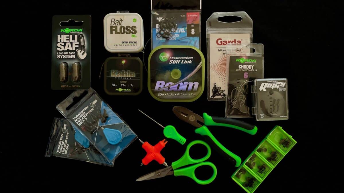 Flat lay of fishing tackle on a black background: packaging for line, lures, hooks, and bright green scissors and pliers.