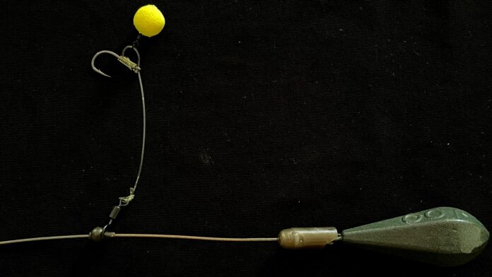 Close-up of fishing tackle: a yellow bobber attached to a curved hook and line against a dark background.