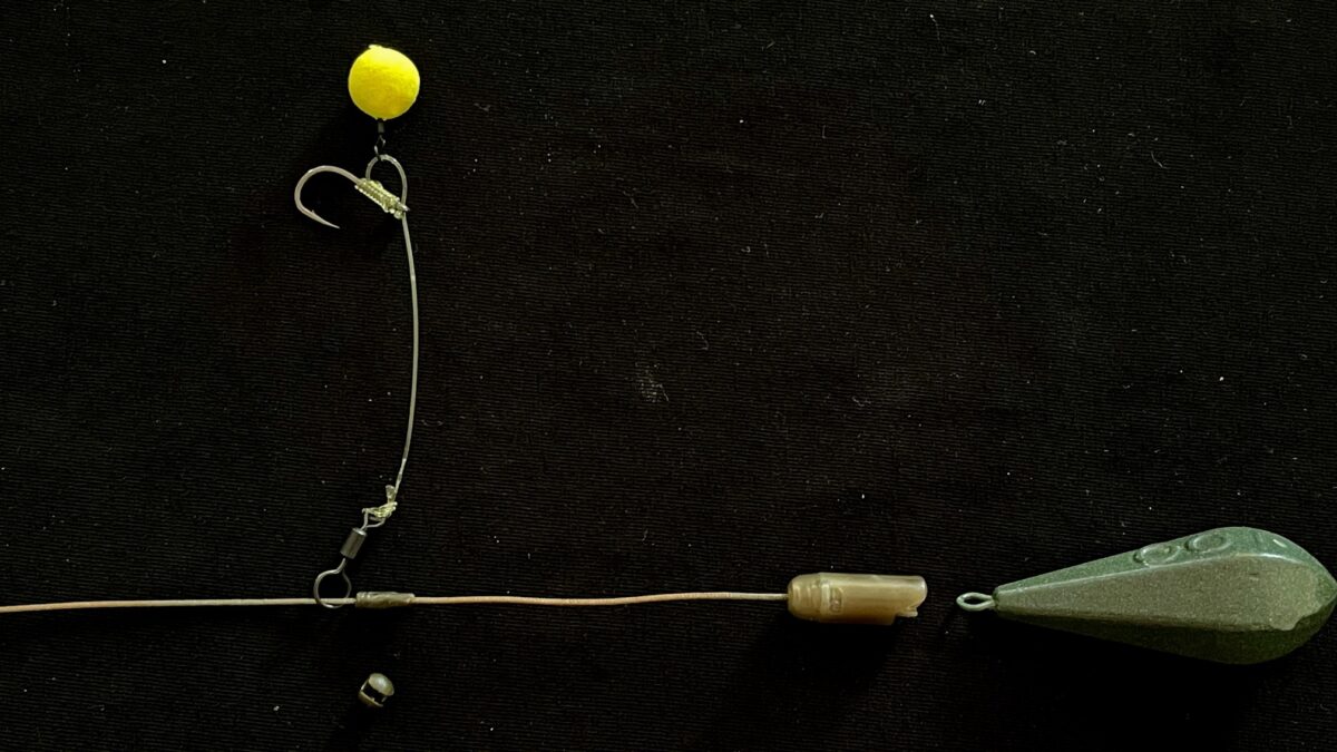 Close-up of a fishing rig with a yellow bobber, hook, and weights on a thin line against a dark background
