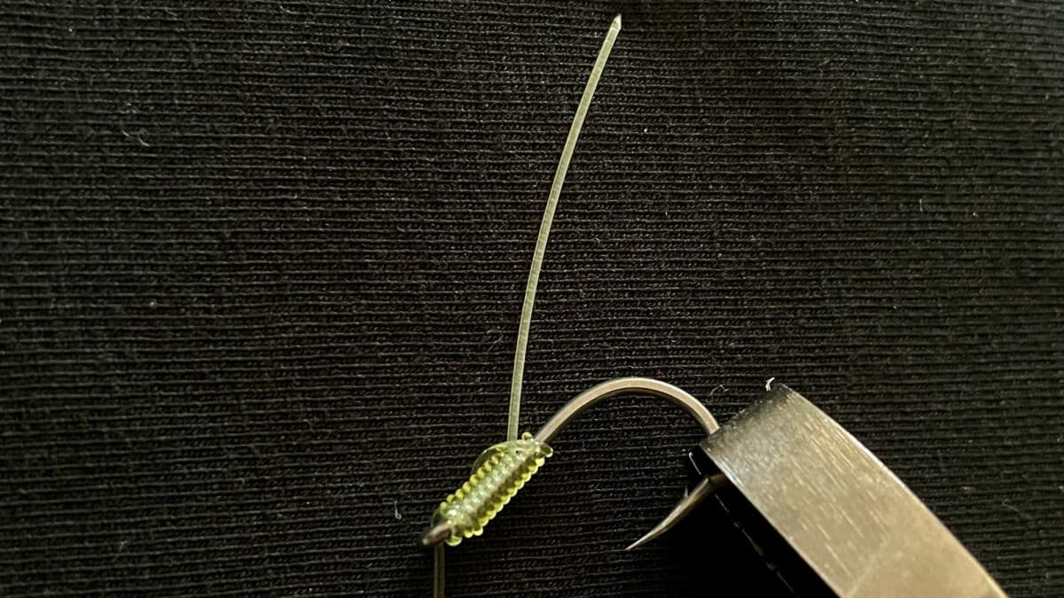 Close-up of a green ribbed plastic fishing lure next to a metal knife blade on a dark textured surface.