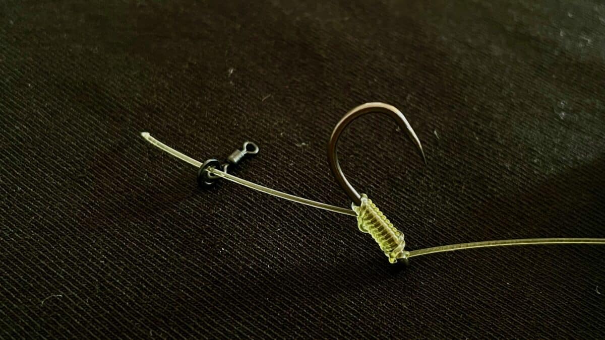 Close-up of a green ribbed curly-tailed fishing lure attached to a curved hook on a dark textured surface.