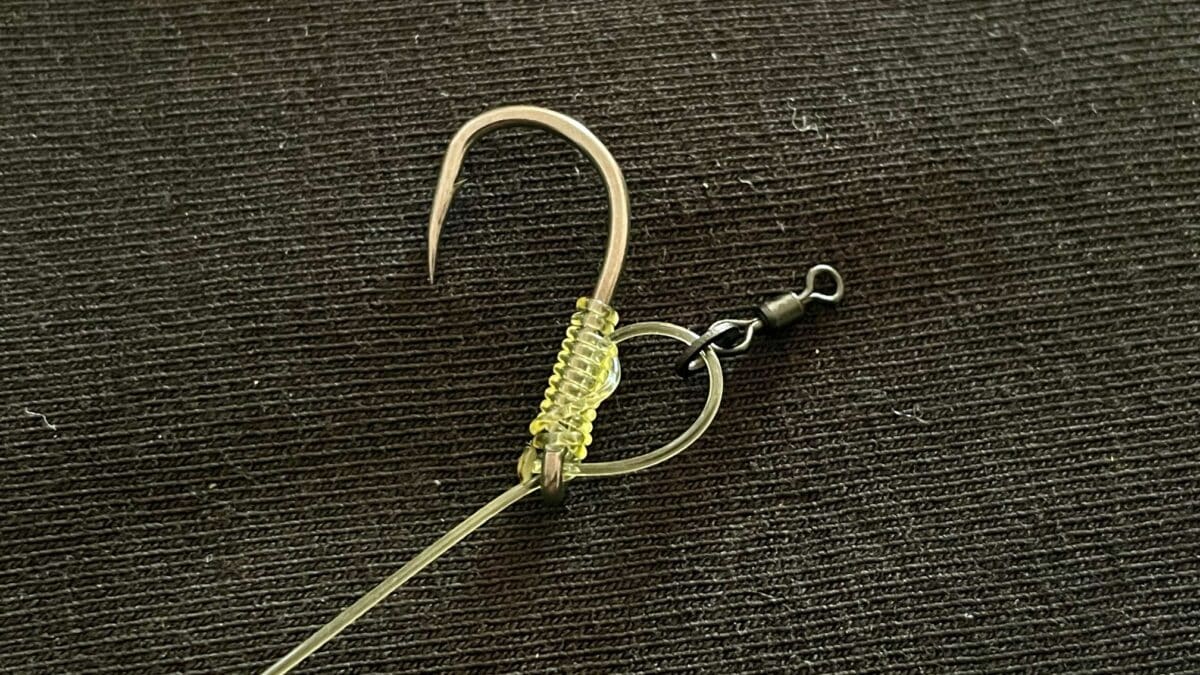 Fishing lure with a curved barbed hook and yellow beaded body on a fishing line.