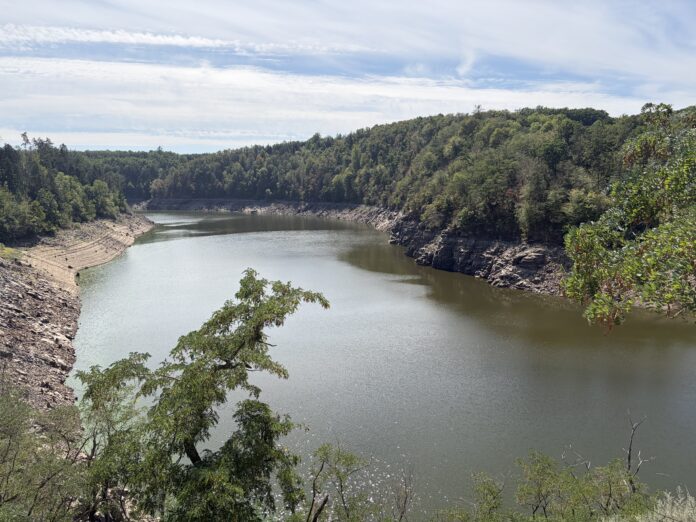 Wide river bends through rocky shoreline and forested hills under a blue sky with wispy clouds.
