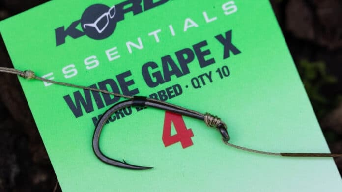 Bright green product tag with bold black text reading 'WIDE GAPE X' and a curved metal fishing lure hook tied with twine over the tag