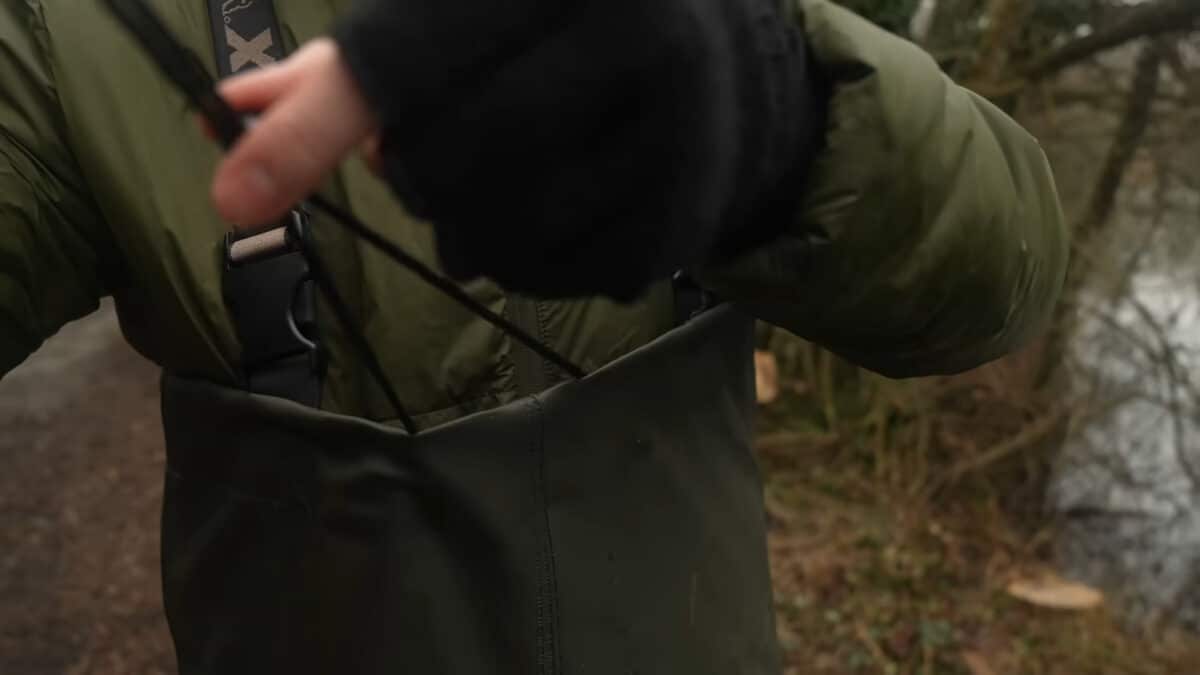 Close-up of a hiker in an olive jacket adjusting a strap on their gear in a forest setting.