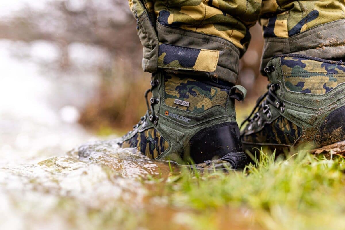 Camouflage military boots standing in muddy water outdoors, showing rugged fabric and laces.