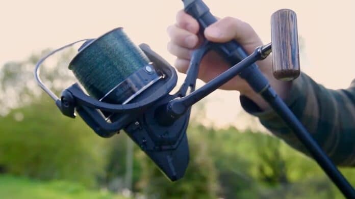 Close-up of a paintball marker with a green hopper being held by a person outdoors in a field.