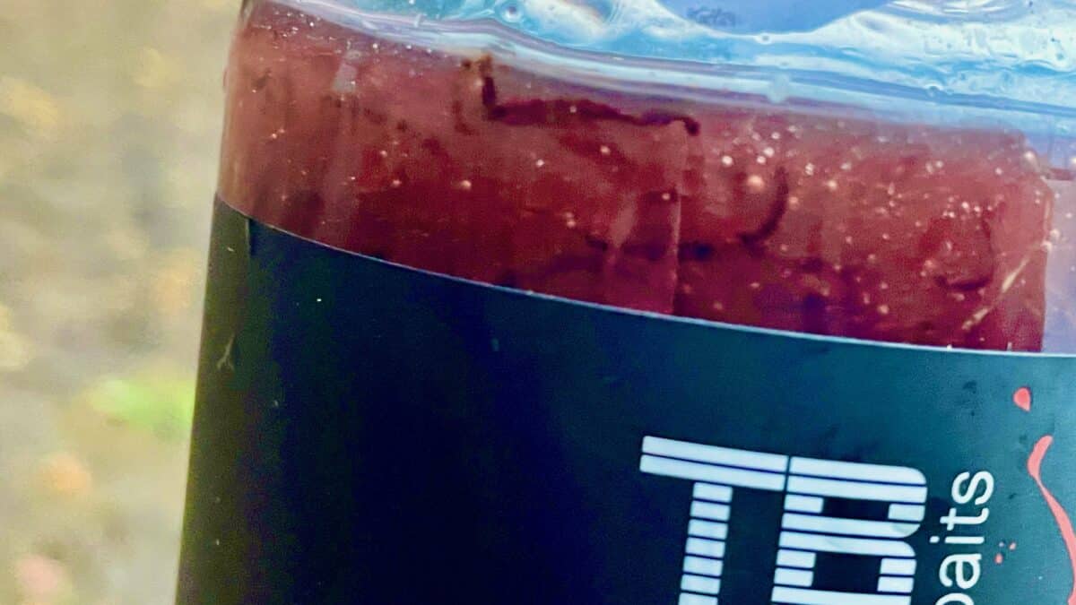 Close-up of a red iced beverage inside a clear plastic cup with ice on top, resting against a dark surface with white text partially visible.