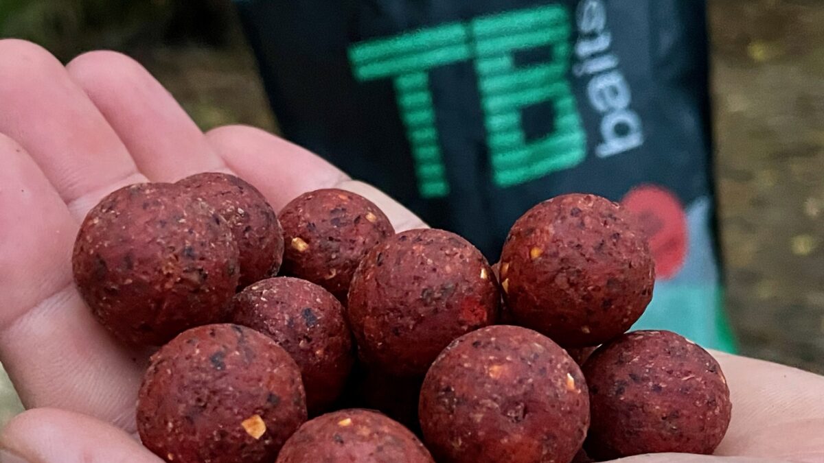 Close-up of red, textured fishing bait balls held in a hand.