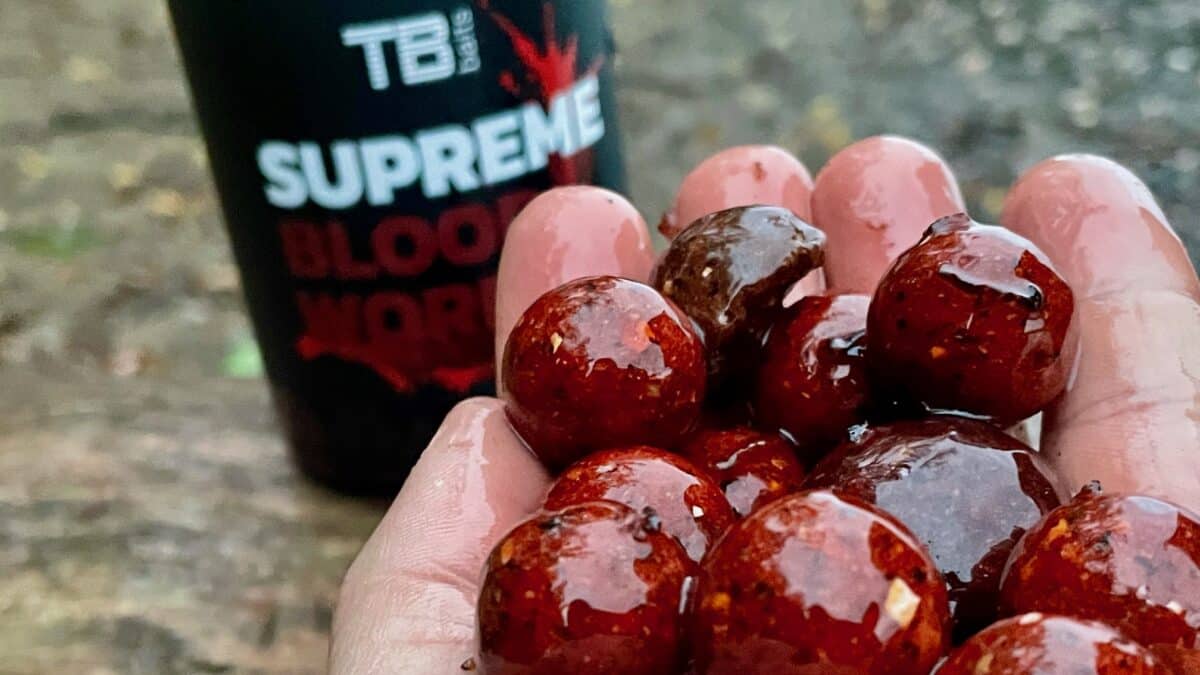 Hand holding glossy red candied grapes with a blurred bottle labeled SUPREME in the background.]','