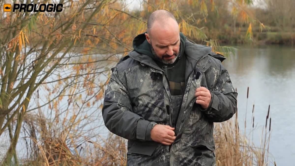 Man in a camo jacket by a lake in autumn, adjusting gear; Prologic Catching Elements logo shows in the top-left corner.