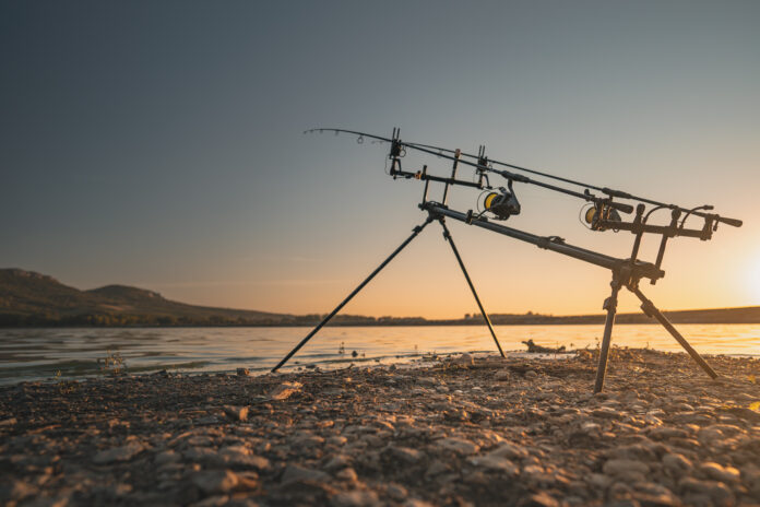 Fishing rods set up on a tripod at the water's edge during sunset/sunrise, ready for casting
