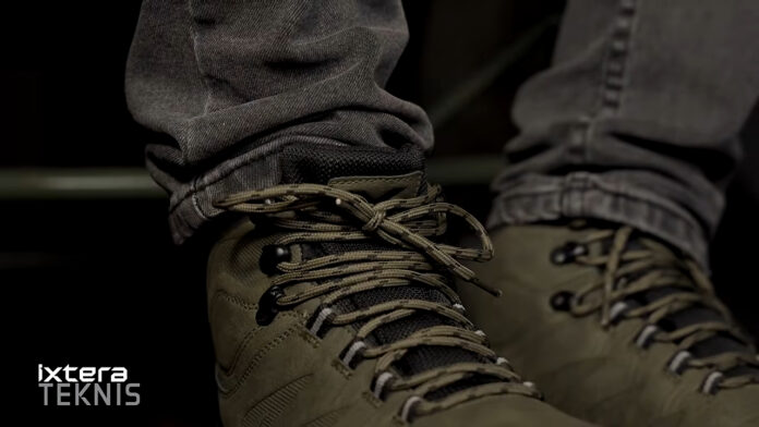 Close-up of olive hiking boots tied with beige laces, pant legs visible, Ixtera Teknis logo in the lower-left corner