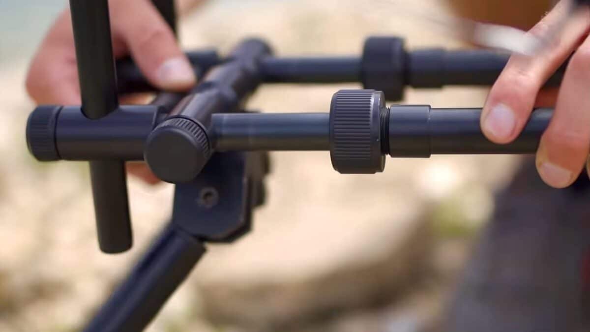 Close-up of hands tightening a knurled knob on a black tripod frame.